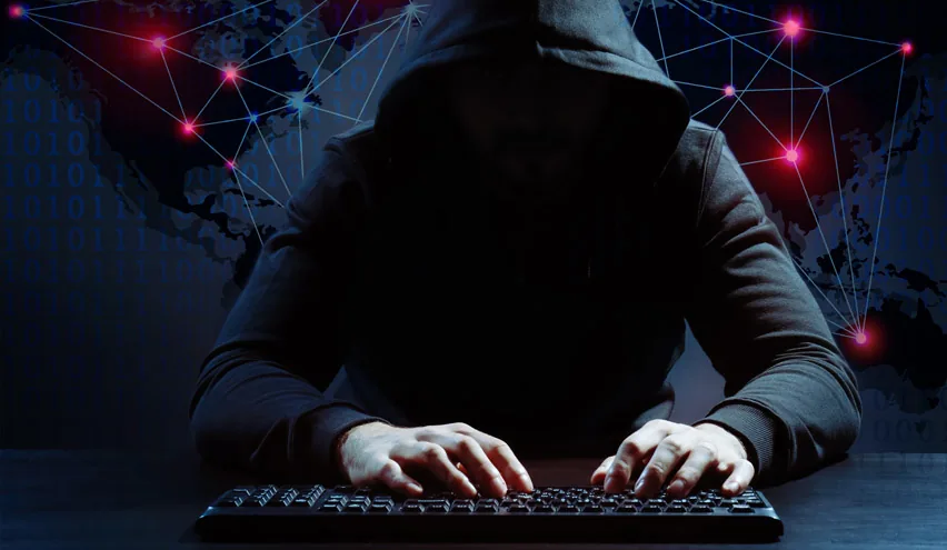 A hooded figure typing at a keyboard in the dark, framed by a glowing world map and a network of connected data points