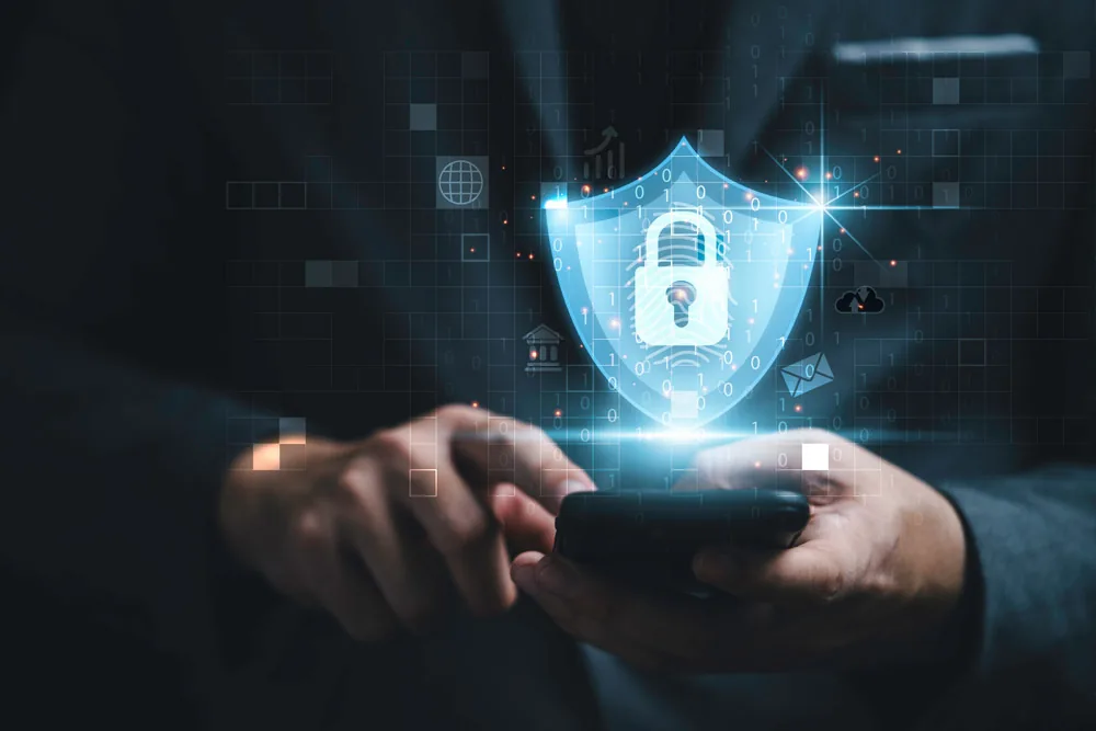 A person holding a smartphone with a glowing digital security shield and padlock icon floating above it, surrounded by binary code and identity data icons